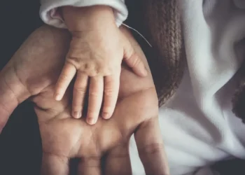 La mano di un neonato appoggiata sul palmo di un adulto, immagine simbolo dell’assegno unico per i figli