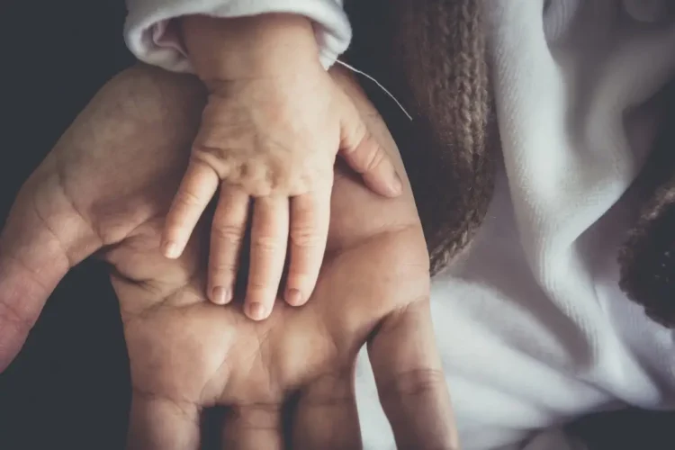 La mano di un neonato appoggiata sul palmo di un adulto, immagine simbolo dell’assegno unico per i figli