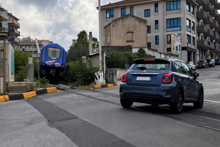 Treno regionale vicino al passaggio a livello di via Paestum a Ragusa mentre un'auto attraversa i binari