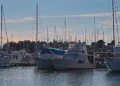 Barche a vela e a motore ormeggiate ai pontili di un porticciolo turistico al tramonto, con il mare in primo piano