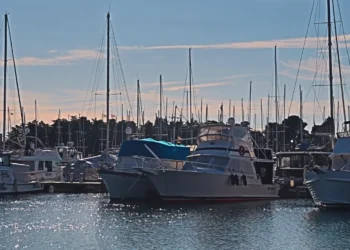 Barche a vela e a motore ormeggiate ai pontili di un porticciolo turistico al tramonto, con il mare in primo piano