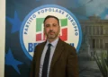 Biagio Pelligra in giacca marrone e cravatta scura davanti al simbolo di Forza Italia e del Partito popolare europeo