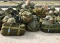 Borsoni militari verdi ed elmetti mimetici dell’esercito ammucchiati a terra, pronti per i volontari, davanti a una staccionata