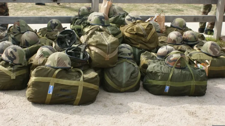 Borsoni militari verdi ed elmetti mimetici dell’esercito ammucchiati a terra, pronti per i volontari, davanti a una staccionata