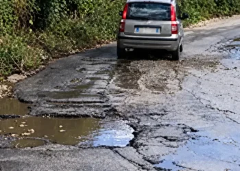 Auto grigia su un tratto dello stradale di Alcerito con asfalto sbriciolato, buche piene d’acqua e crepe lungo la carreggiata