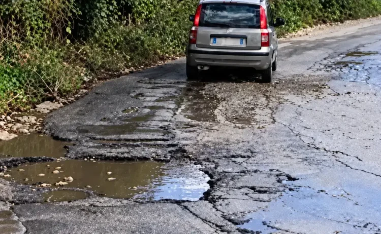 Auto grigia su un tratto dello stradale di Alcerito con asfalto sbriciolato, buche piene d’acqua e crepe lungo la carreggiata
