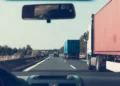 Camion con container rosso e autoarticolato blu in viaggio su un’autostrada, ripresi dall’interno di un’auto
