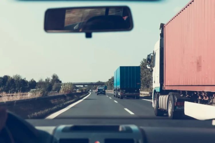 Camion con container rosso e autoarticolato blu in viaggio su un’autostrada, ripresi dall’interno di un’auto