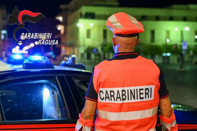 Un carabiniere visto di spalle, con pettorina e berretto arancioni, accanto a un’auto di servizio durante un controllo serale