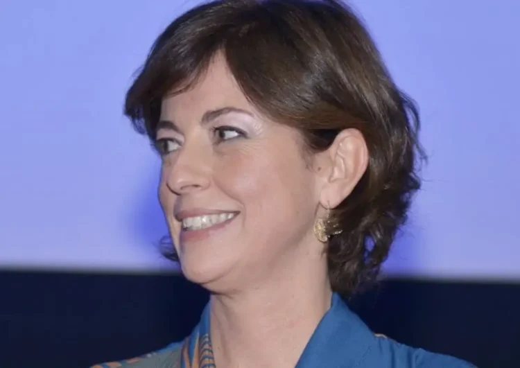 Carlotta Schininà, socia di Anele e sostenitrice del film su Biagio Conte, sorride di profilo con camicia blu e orecchini dorati