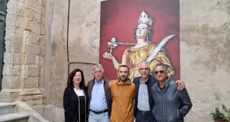 Cinque persone in posa nel cortile della chiesa di Santa Lucia a Modica, davanti a un pannello con la statua della santa