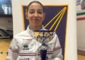 Giovane schermitrice della Conad Scherma Modica in tuta bianca con una coppa argentata, davanti a un pannello blu e giallo