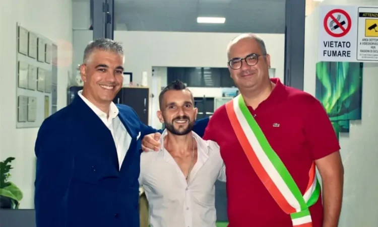 Daniele Spadola sorridente tra due uomini all’inaugurazione della sua palestra a Ispica, uno con la fascia tricolore