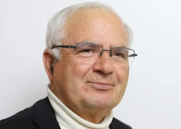 Ritratto di don Giovanni Mandarà con occhiali, dolcevita bianco e giacca scura su sfondo chiaro