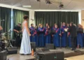 Elma Rizza, in abito azzurro, canta nel giorno della laurea a Messina, davanti al coro in tunica blu e alla band