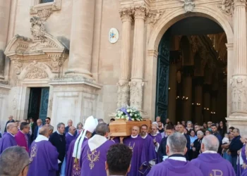 Sacerdoti in paramenti viola portano la bara di don Salvatore Dinatale fuori dalla cattedrale di Ragusa, tra i fedeli