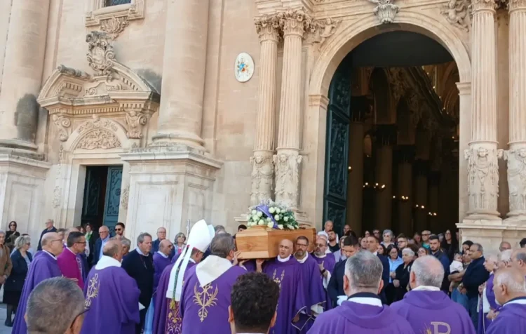 Sacerdoti in paramenti viola portano la bara di don Salvatore Dinatale fuori dalla cattedrale di Ragusa, tra i fedeli