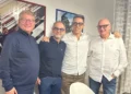 Quattro uomini sorridenti in posa abbracciati in una stanza, per le nuove adesioni al MpA a Comiso