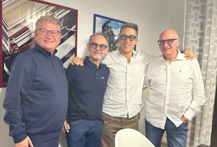 Quattro uomini sorridenti in posa abbracciati in una stanza, per le nuove adesioni al MpA a Comiso