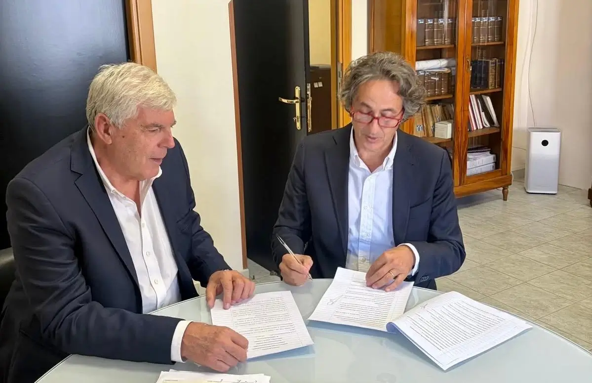 Due uomini in giacca firmano documenti a un tavolo di vetro: incarico per la Psichiatria 1 Ragusa-Vittoria