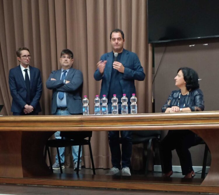 Documenti firmati su un tavolo, sullo sfondo l’aeroporto di Comiso