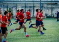 Calciatori del Frigintini Calcio in maglia rossa e pantaloncini blu corrono in allenamento su un campo in erba sintetica