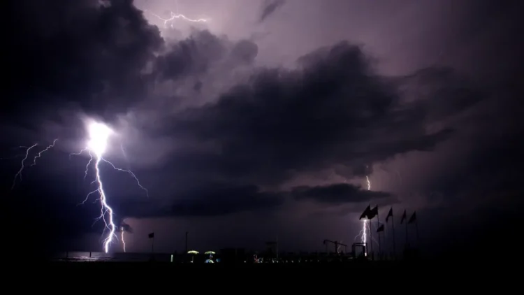 Fulmini cadono sul mare di notte vicino a uno stabilimento balneare, cielo temporalesco: allerta meteo in Sicilia