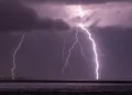 Fulmini che scendono sul mare durante un temporale notturno, con le luci di un tratto di costa sullo sfondo: maltempo