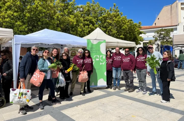 Soci del GAS Mazzarelli in felpa bordeaux posano in piazza tra i gazebo, con ortaggi freschi e borse della spesa