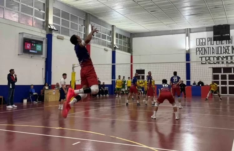 Giocatore del Giarratana Volley in maglia blu e pantaloncini rossi salta per la battuta in una palestra durante una gara