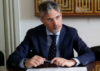 Giovanni Iacono, assessore uscente a Ragusa, in giacca blu e cravatta a pois seduto a un tavolo con una penna tra le mani