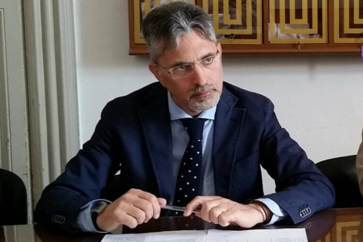 Giovanni Iacono, assessore uscente a Ragusa, in giacca blu e cravatta a pois seduto a un tavolo con una penna tra le mani