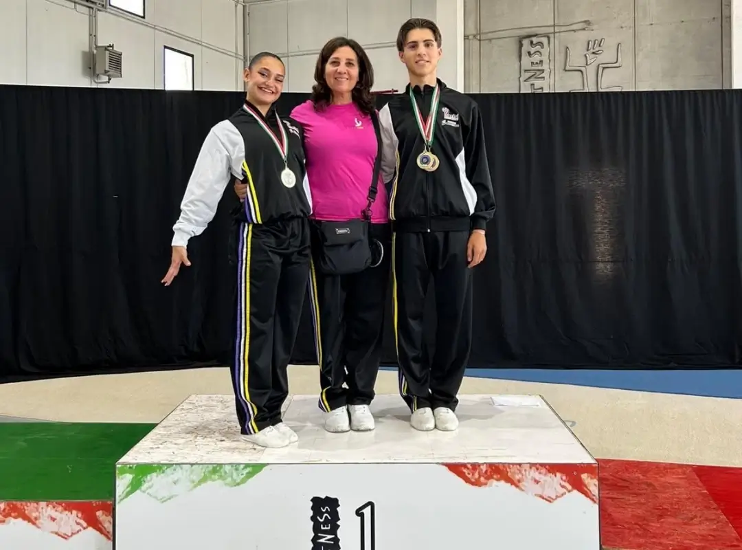 Due atleti di ginnastica aerobica della Motyka Modica con le medaglie sul gradino più alto del podio, accanto all’istruttrice