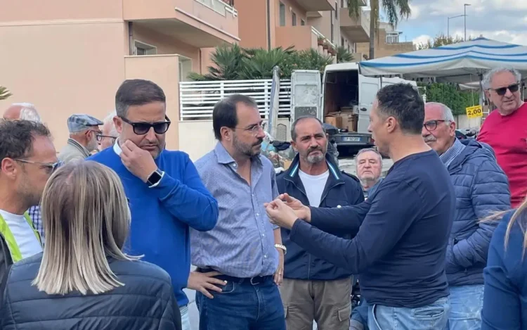 Rappresentanti politici e ambulanti a confronto in strada al mercato del venerdì di Comiso, accanto a un furgone e a una bancarella