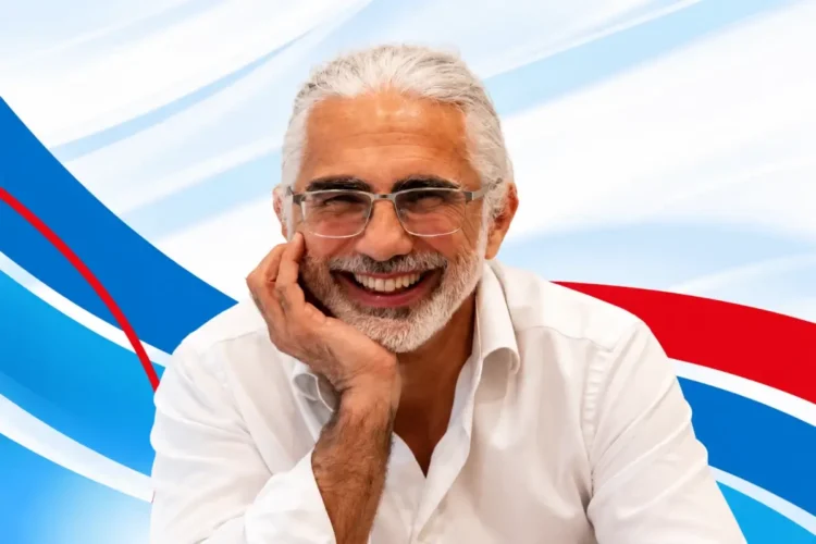 Luigi Santapaga, formatore della giornata AVIS Modica per i docenti, sorride con la mano sul viso su sfondo blu e rosso