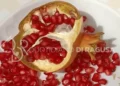 Melograno aperto a metà su un piatto bianco, con i chicchi rossi sparsi tutto intorno