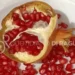 Melograno aperto a metà su un piatto bianco, con i chicchi rossi sparsi tutto intorno