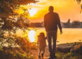 Padre e figlio piccolo di spalle camminano verso un lago al tramonto, immagine sull’assegno unico per le famiglie