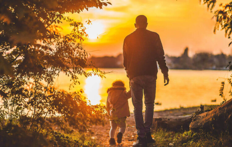 Padre e figlio piccolo di spalle camminano verso un lago al tramonto, immagine sull’assegno unico per le famiglie