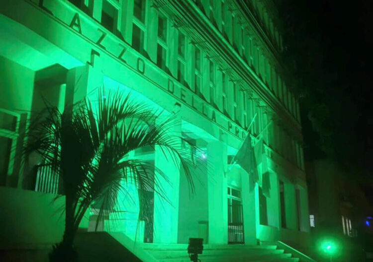 Facciata del Palazzo della Provincia di Ragusa illuminata di verde per la fibrosi cistica, con una palma davanti all’ingresso