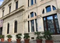 Facciata in pietra di un palazzo del centro storico di Modica, con finestre ad arco, vetrate e palme in vaso all’ingresso