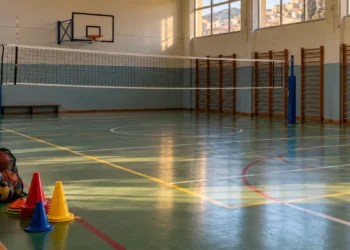 Palestra scolastica vuota a Ragusa con canestro, rete da pallavolo e parquet. Immagine generata con intelligenza artificiale.
