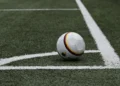 Pallone da calcio bianco con strisce nere, rosse e gialle fermo vicino alla bandierina del calcio d’angolo su un campo in erba sintetica