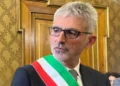 Il sindaco di Ragusa Peppe Cassì, a capo della giunta, con fascia tricolore e occhiali davanti a una porta in legno