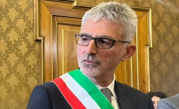 Il sindaco di Ragusa Peppe Cassì, a capo della giunta, con fascia tricolore e occhiali davanti a una porta in legno