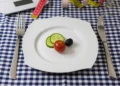 Piatto con due fette di cetriolo, un pomodorino e un’oliva, tra metri da sarta e bilancia: una cena ridotta per dimagrire