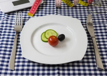 Piatto con due fette di cetriolo, un pomodorino e un’oliva, tra metri da sarta e bilancia: una cena ridotta per dimagrire