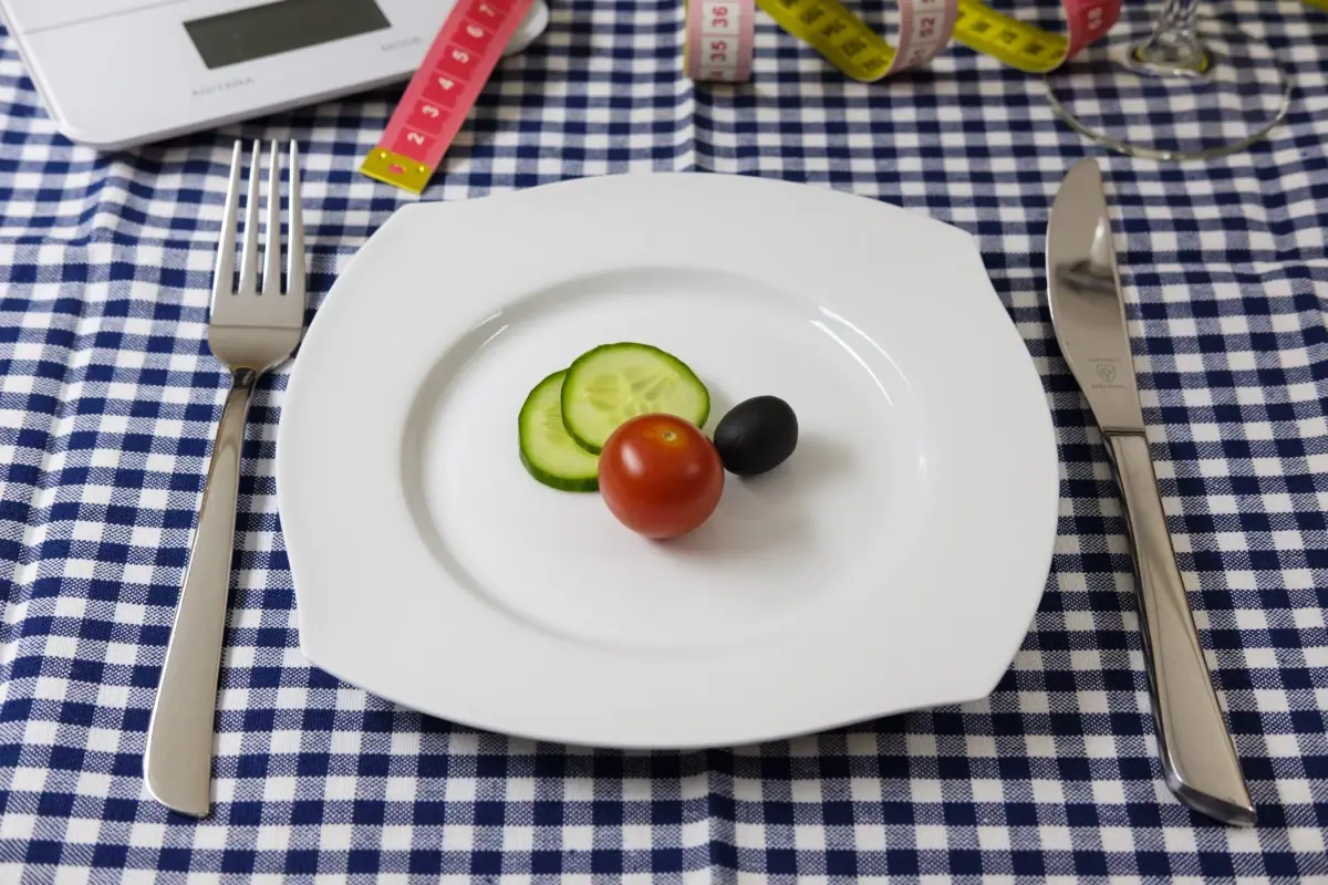 Piatto con due fette di cetriolo, un pomodorino e un’oliva, tra metri da sarta e bilancia: una cena ridotta per dimagrire
