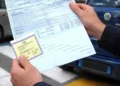 Mani di un uomo con il modulo di una polizza auto e il contrassegno assicurativo giallo, davanti a un’auto parcheggiata