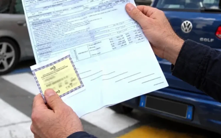 Mani di un uomo con il modulo di una polizza auto e il contrassegno assicurativo giallo, davanti a un’auto parcheggiata